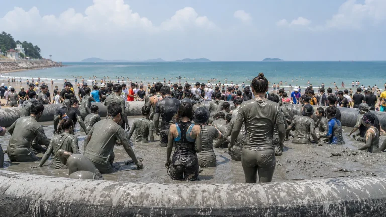 Adults enjoying a mud activity zone at a Korean summer beach festival.