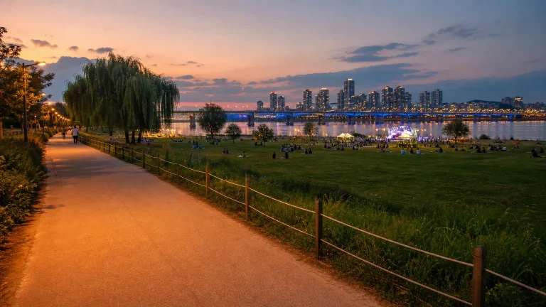 Evening view of people relaxing beside Seoul Han River with a bridge in the background